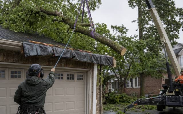 Crane lifting a storm-broken limb off a tarped garage roof in the rain